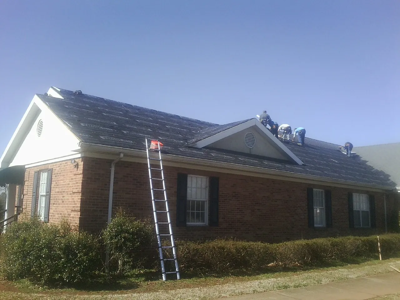 Crew tearing shingles off a brick ranch roof with a ladder set — Metal Roof Repair work by our crew in Paeonian Springs