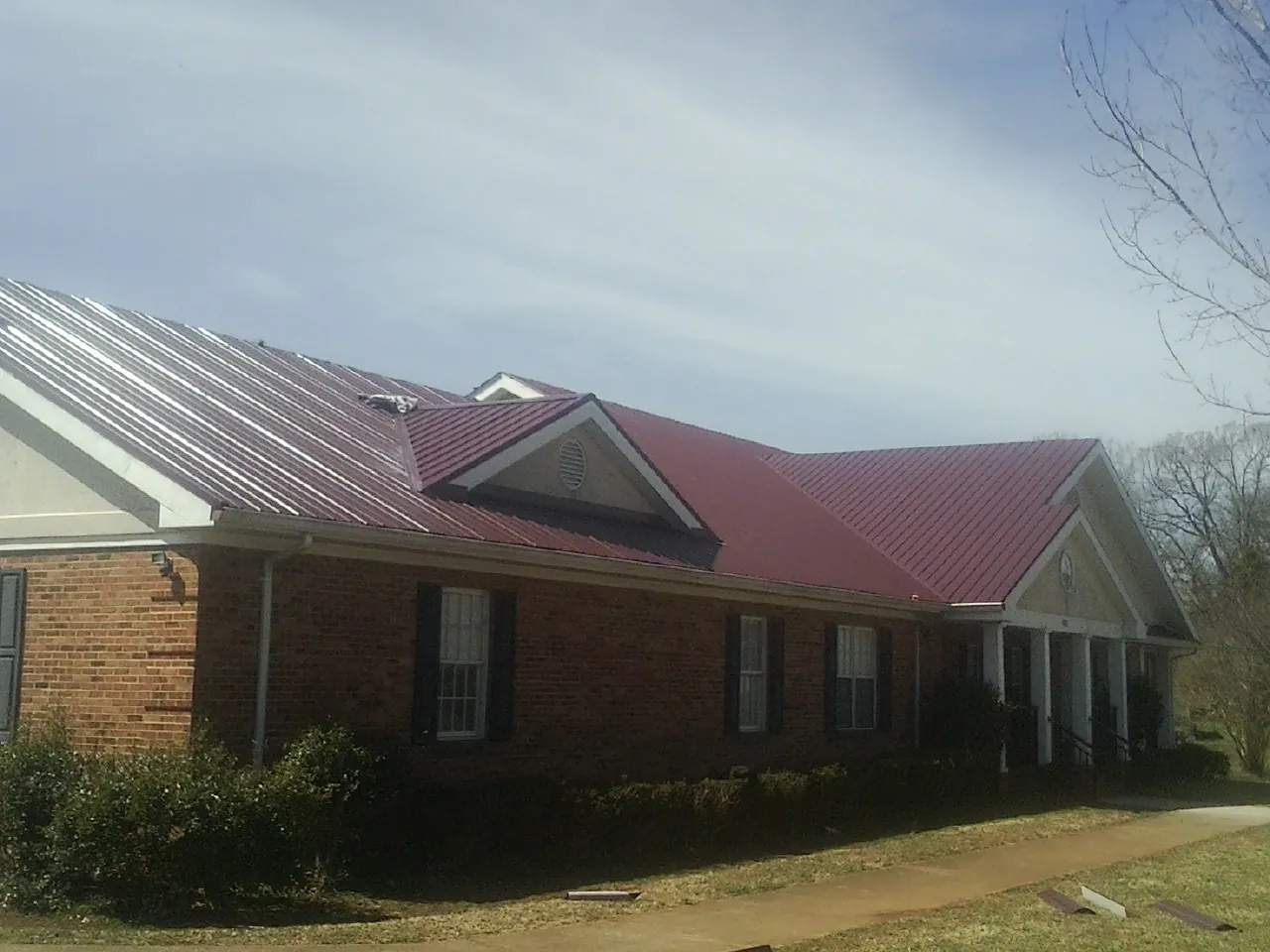 Red metal roof with gabled entries on a long brick building, from a Hail Damage Roof Repair job in Paeonian Springs