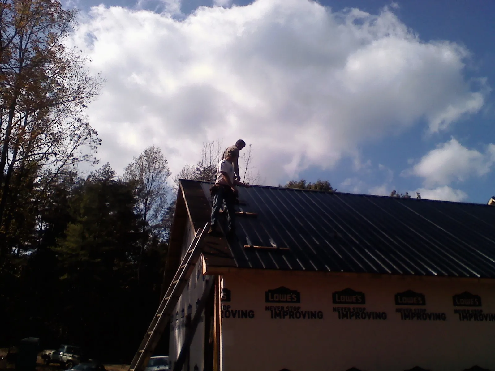 Roofer fastening dark metal panels high against a cloudy sky, from a Roof Inspection job in Paeonian Springs