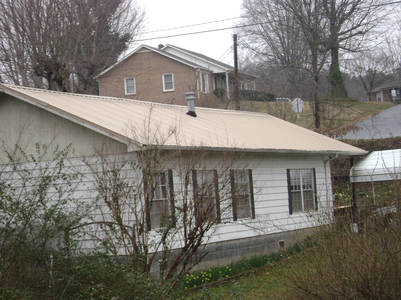 Tan metal roof on a white sided house set into a hillside — Commercial Roofing by Roofing Brothers in Paeonian Springs